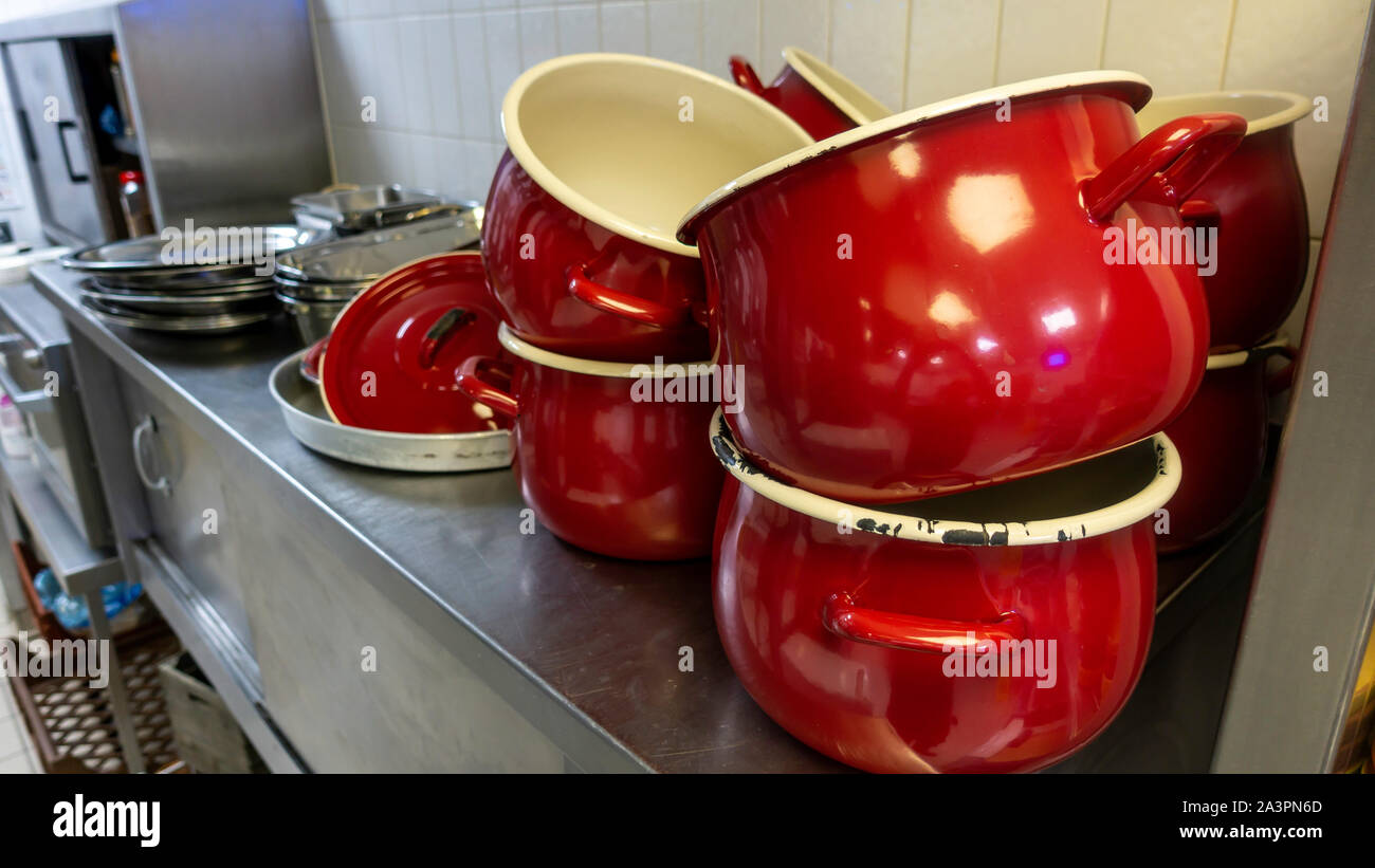 Vecchio rosso scheggiato pentole nella cucina industriale con altri utensili da cucina Foto Stock