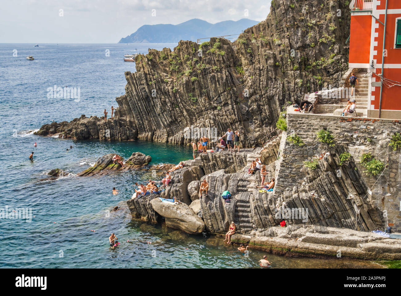 Riomaggiore Cinque Terre, Italia - Agosto 17, 2019: la gente a prendere il sole sulle rocce, spiaggia vacanze sulla costa del Mar Ligure. Montagne Foto Stock