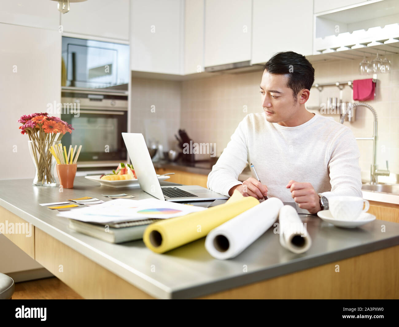 Giovani asiatici free lance designer seduti al bancone cucina creando un progetto utilizzando la pen tablet e computer laptop. Foto Stock