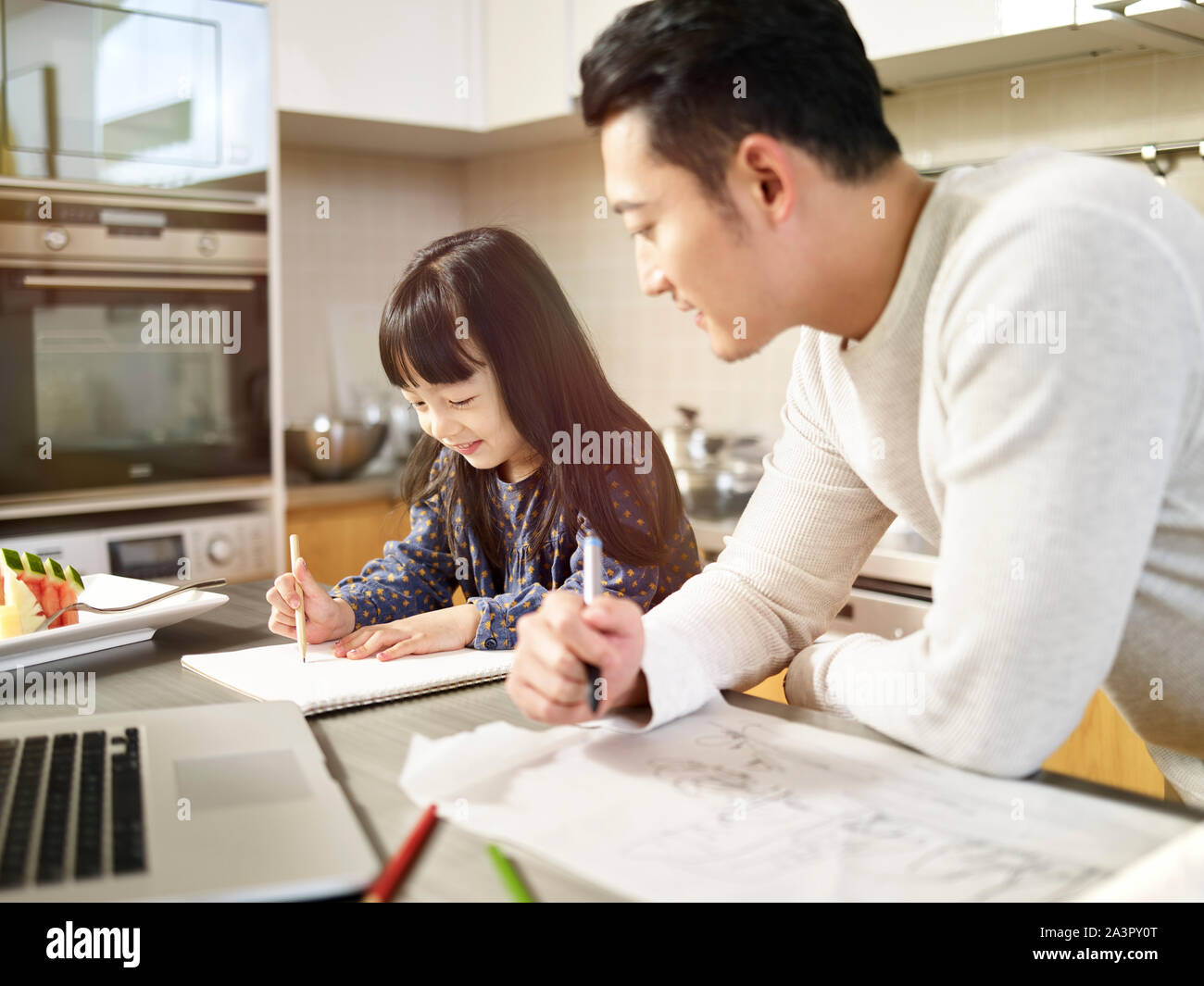 Giovane uomo asiatico free lance designer padre lavora a casa mentre si prende cura della figlia. Foto Stock