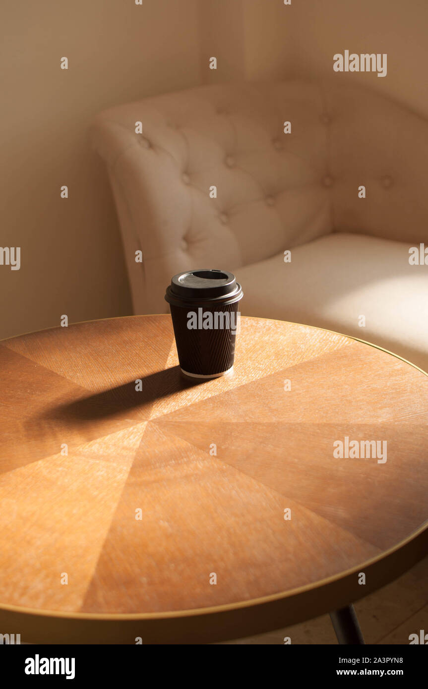 Una tazza monouso di caffè su un tavolo in legno con interni sunbeam Foto Stock