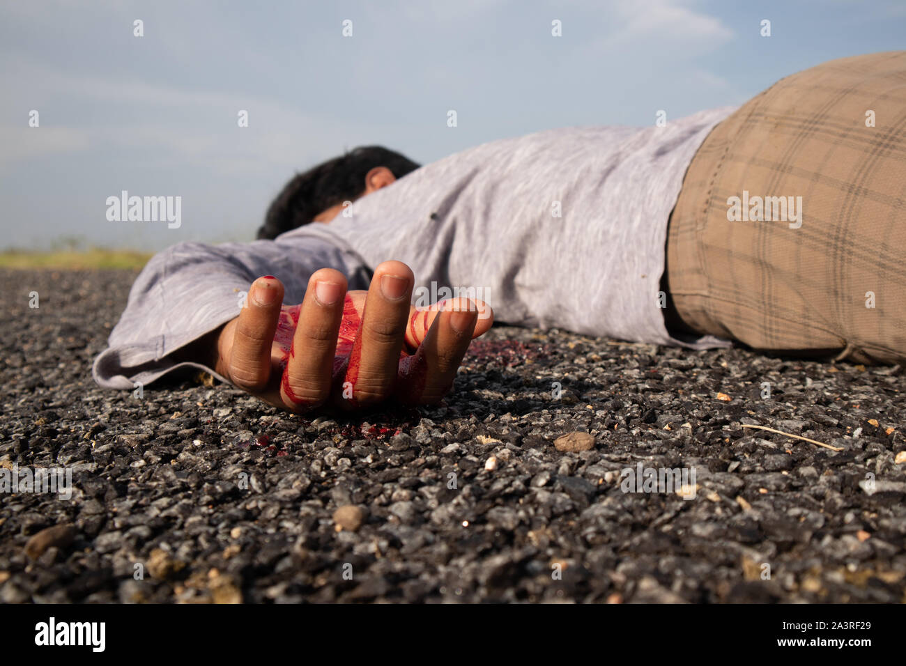 Concetto della scena del crimine ,il fuoco selettivo alla vittima la mano con il sangue di un corpo morto posa sulla strada. Foto Stock