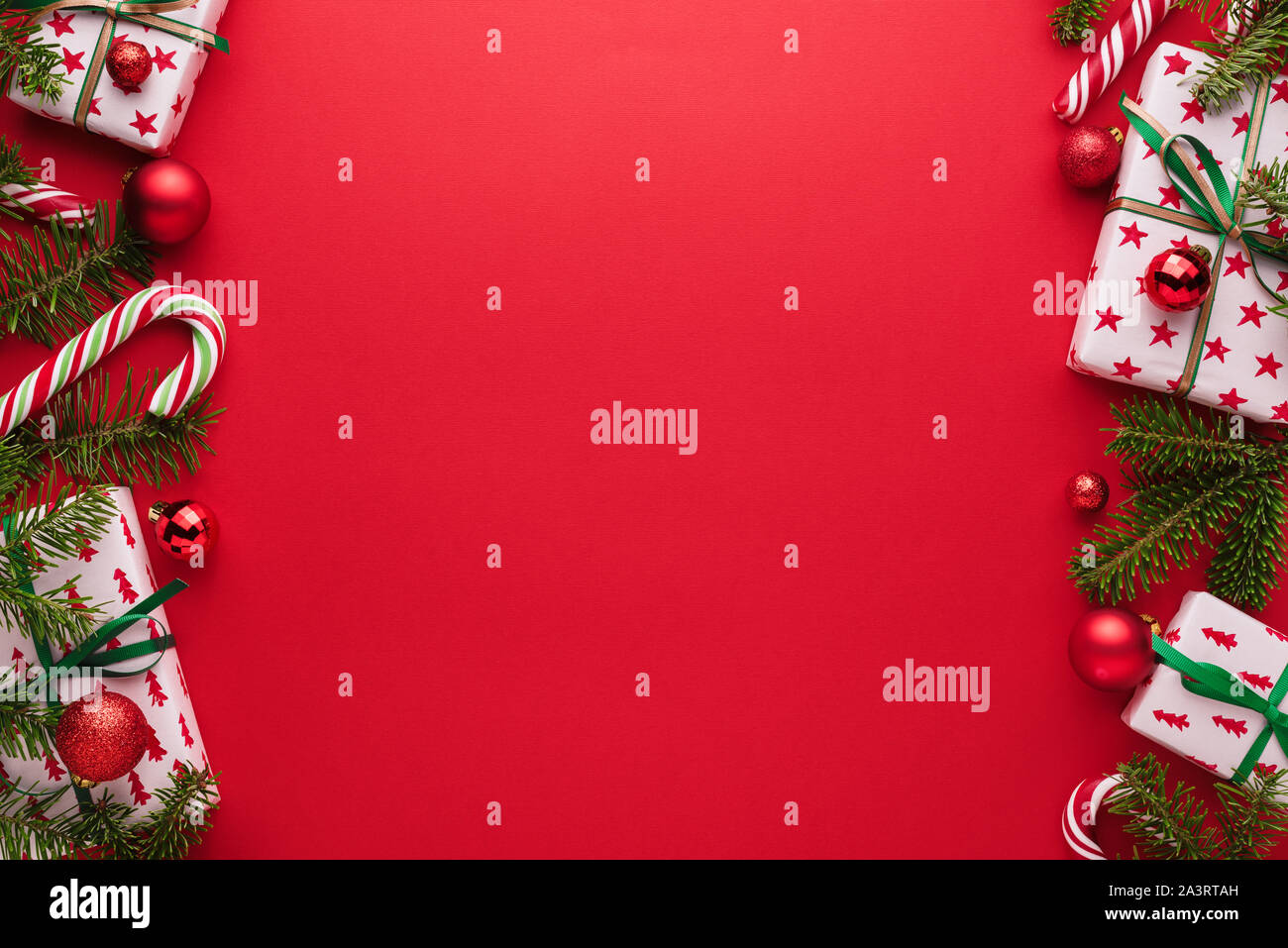 Sfondo rosso per il Natale di creep. Confine di rami di abete, confezioni regalo, palle di Natale e candy cane Foto Stock