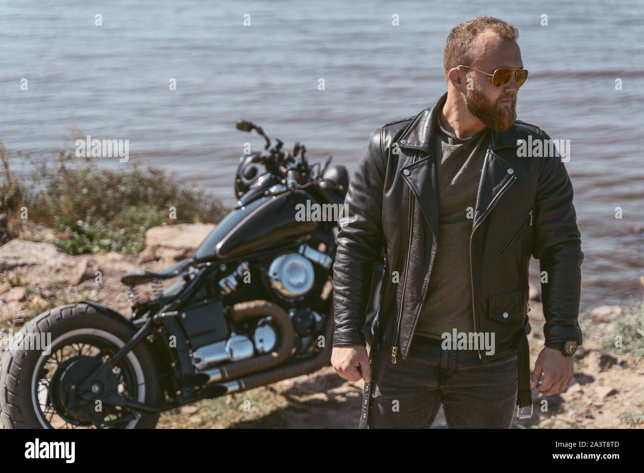 Bello barbuto biker in posa vicino alla sua motocicletta Foto Stock