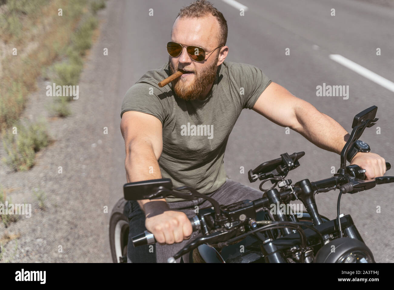 Bello barbuto biker seduto sulla bici sigar fumare sulla strada Foto Stock