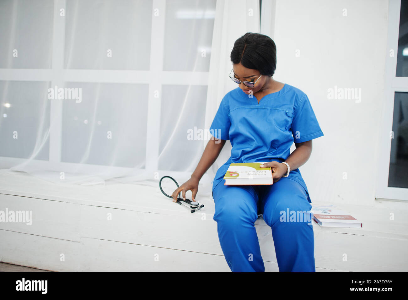 Ritratto di donna felice americano africano giovane medico pediatra in uniforme blu e il cappotto di uno stetoscopio con libri a mani. Sanitario, medico, med Foto Stock