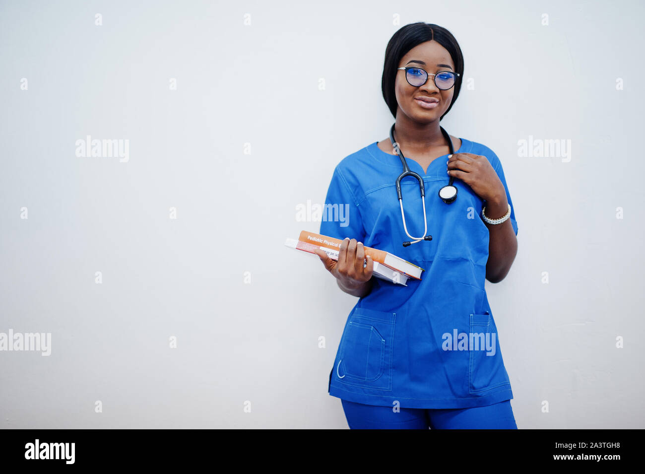 Ritratto di donna felice americano africano giovane medico pediatra in uniforme blu e il cappotto di uno stetoscopio con libri a mani isolato su bianco. Foto Stock