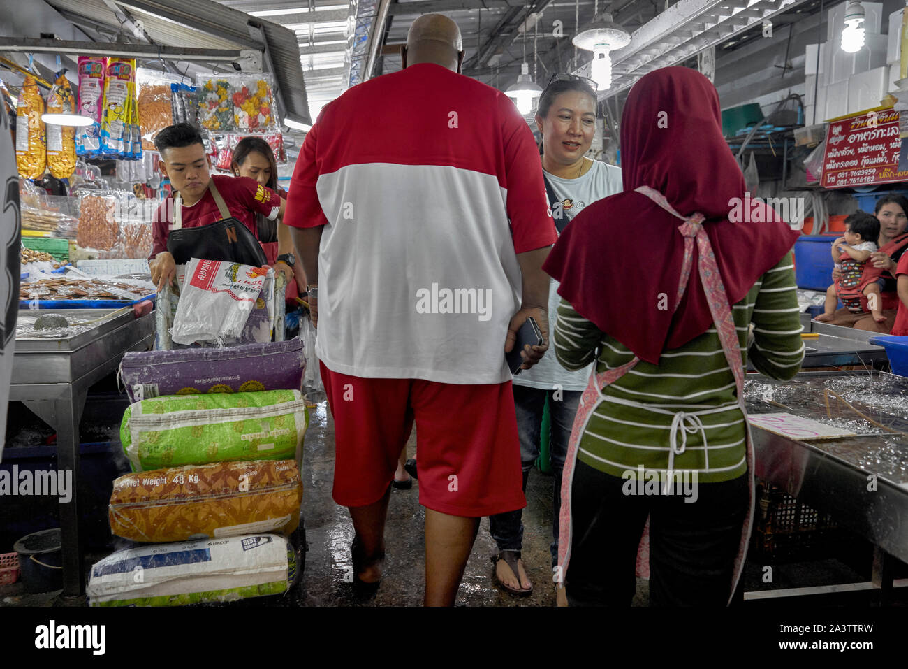 Grande uomo a piedi attraverso lo spazio confinato di un mercato stretto vicolo che fornisce accesso limitato ad altre persone. Thailandia Mercato, sud-est asiatico Foto Stock