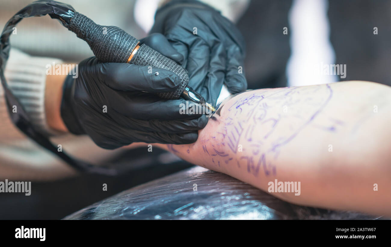 Professional tattoo artist fa un tatuaggio su una giovane mano d'uomo, close-up. Tattoo Artist facendo tattoo nel salone di tatuaggi. Processo di fabbricazione di un tatuaggio in compagnia TAT European Airlines Foto Stock