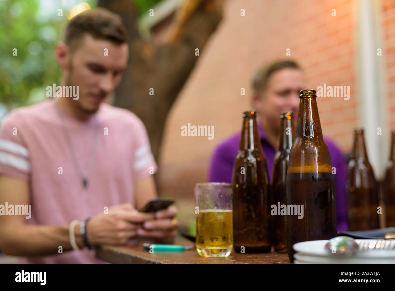 Felice l'uomo seduto e utilizzando il telefono all'aperto pur avendo la birra la messa a fuoco su oggetti in primo piano Foto Stock