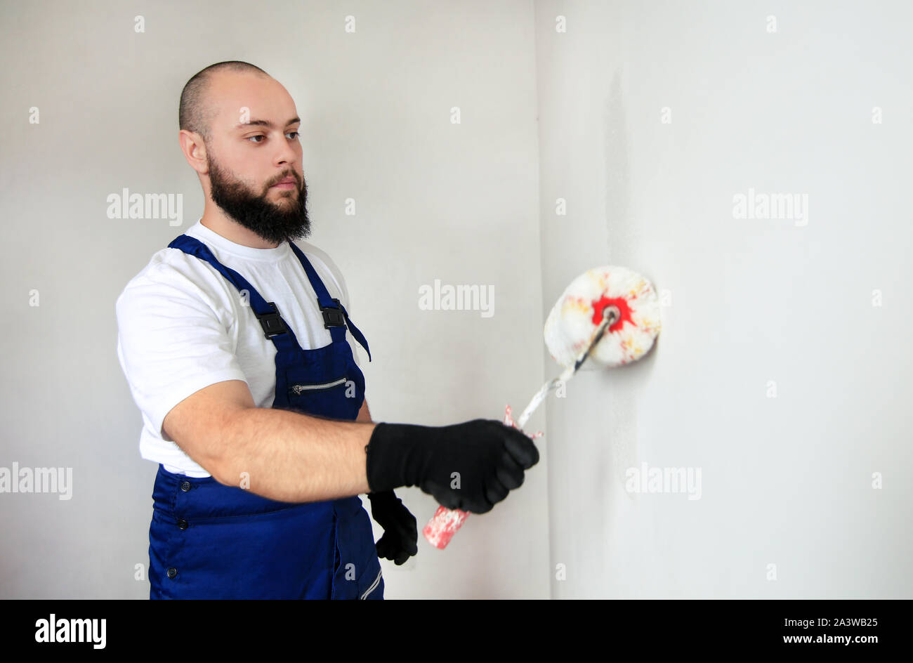 Operaio edile finitura facendo lavori di rinnovo nell'appartamento. Pittore professionista contraente utilizzando vernice bianca spazzola a rullo pittura del muro di cemento. Foto Stock
