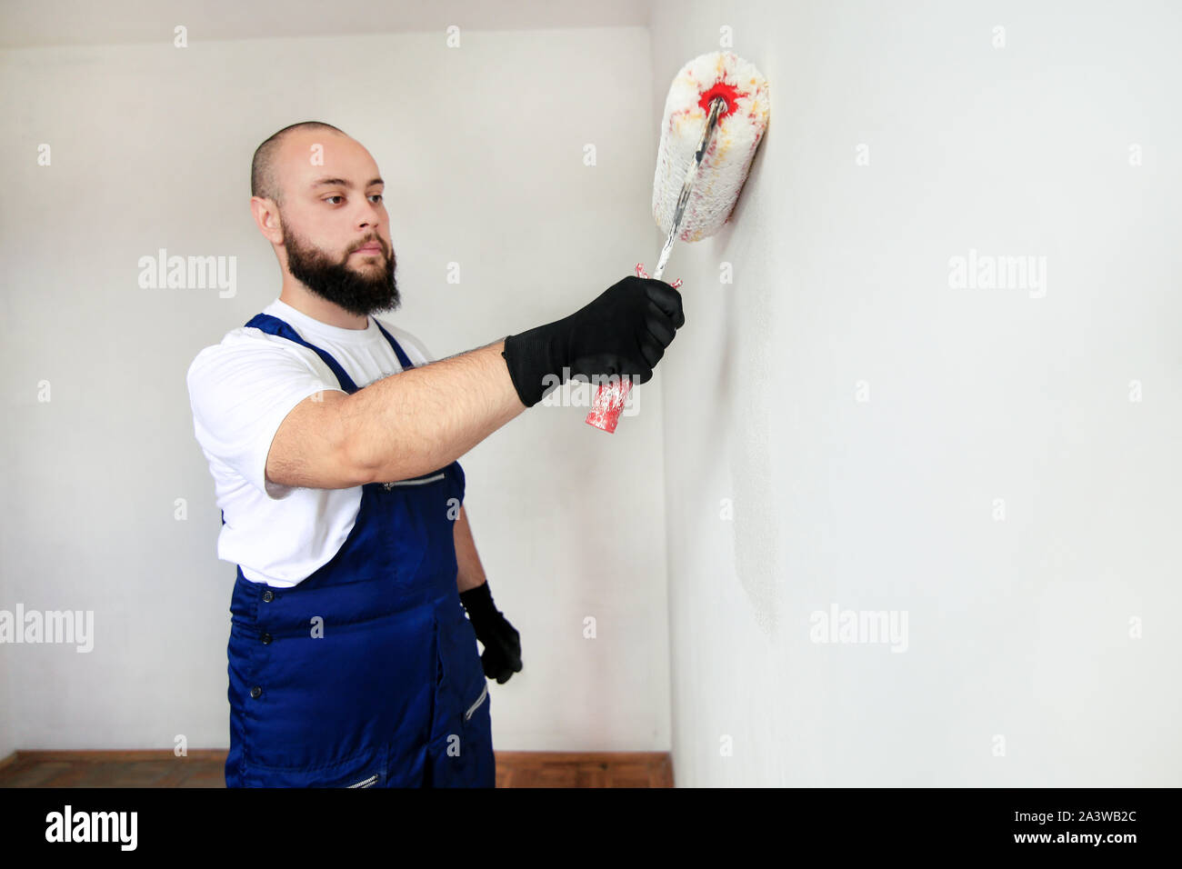 Operaio edile finitura facendo lavori di rinnovo nell'appartamento. Pittore professionista contraente utilizzando vernice bianca spazzola a rullo pittura del muro di cemento. Foto Stock