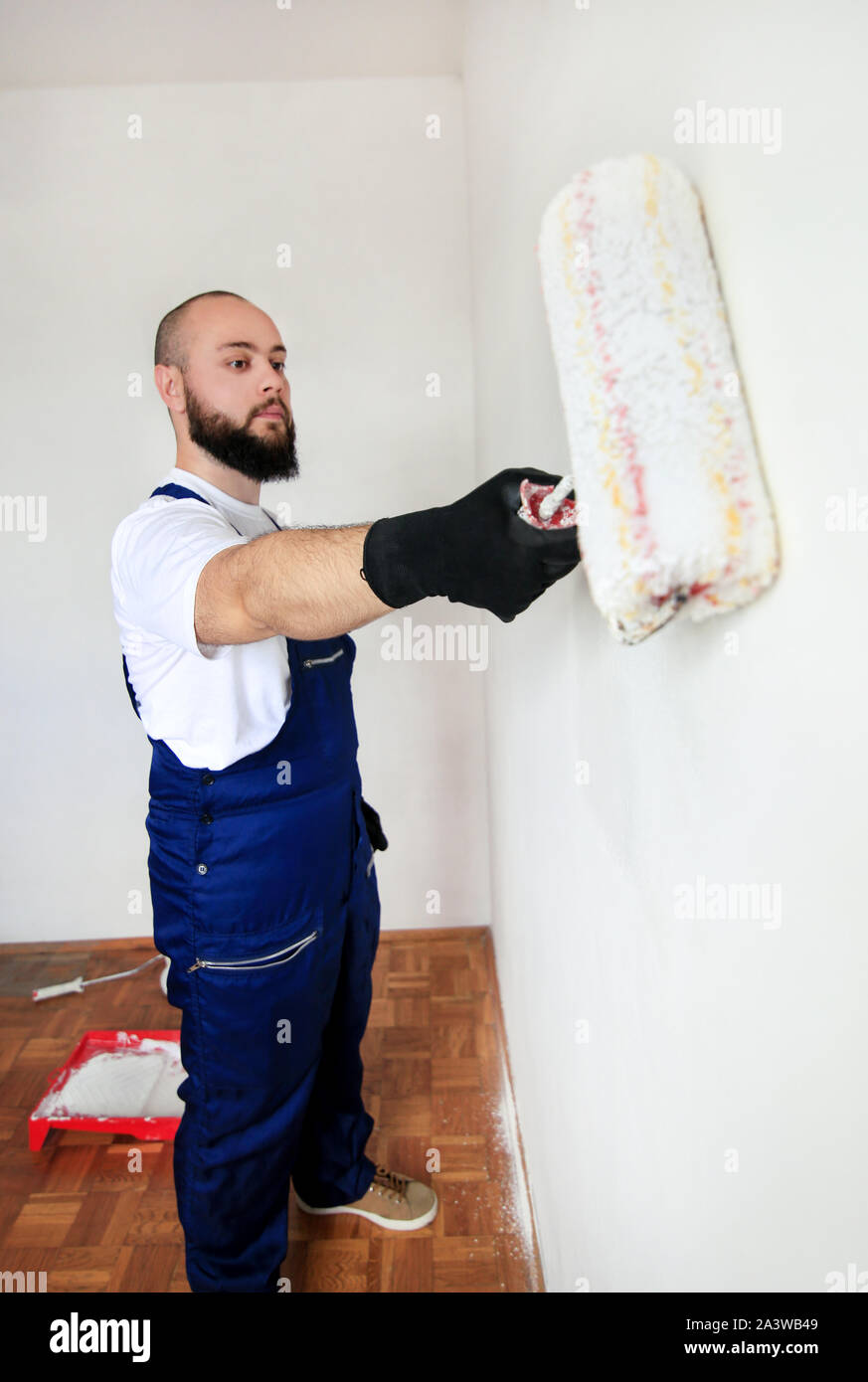 Operaio edile finitura facendo lavori di rinnovo nell'appartamento. Pittore professionista contraente utilizzando vernice bianca spazzola a rullo pittura del muro di cemento. Foto Stock