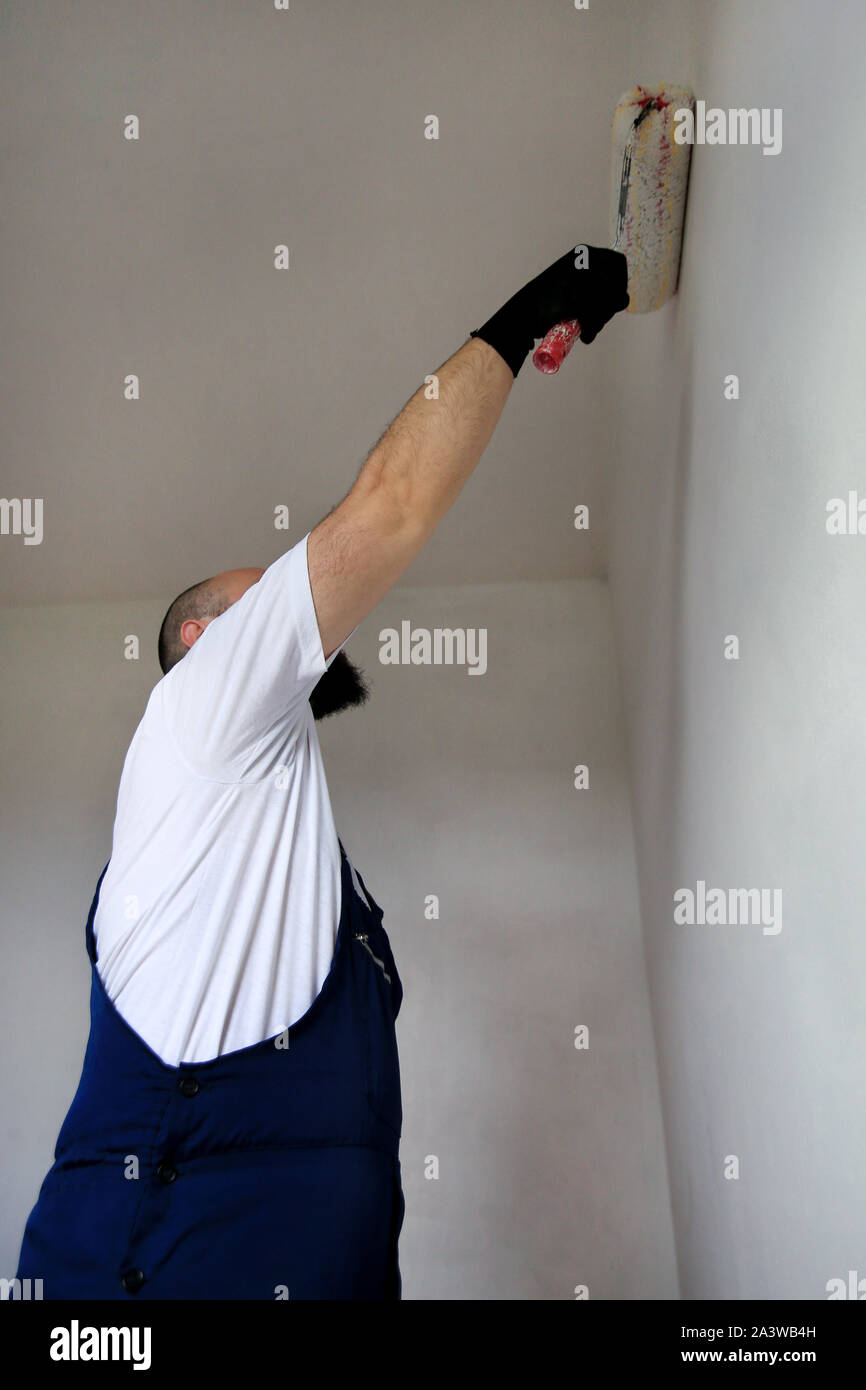 Operaio edile finitura facendo lavori di rinnovo nell'appartamento. Pittore professionista contraente utilizzando vernice bianca spazzola a rullo pittura del muro di cemento. Foto Stock