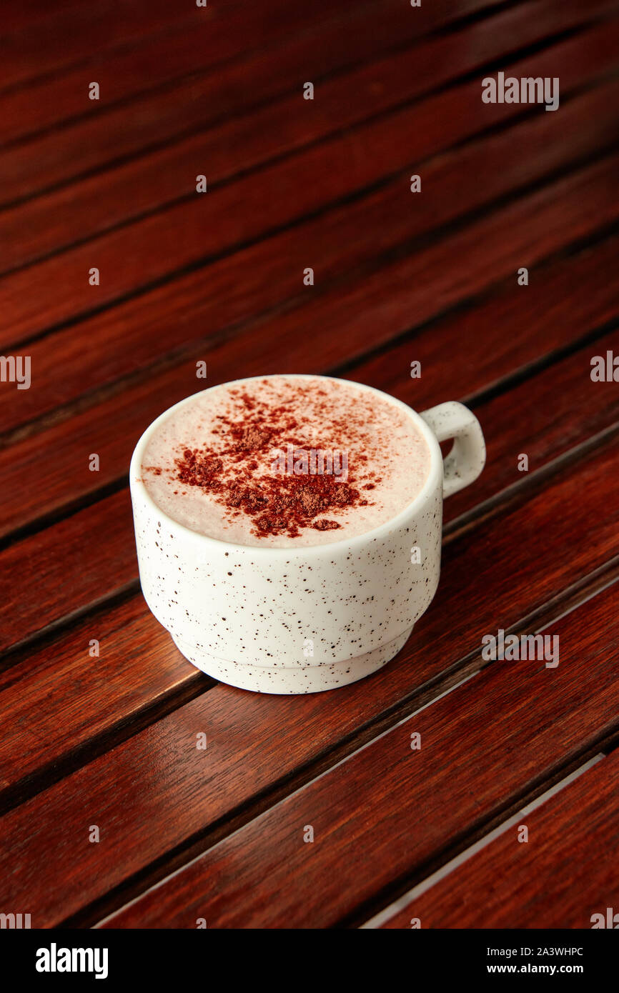 Tazza di cioccolata calda con schiuma di latte e una spruzzata di cacao su un tavolo di legno su sfondo marrone. Con copyspace. Foto Stock