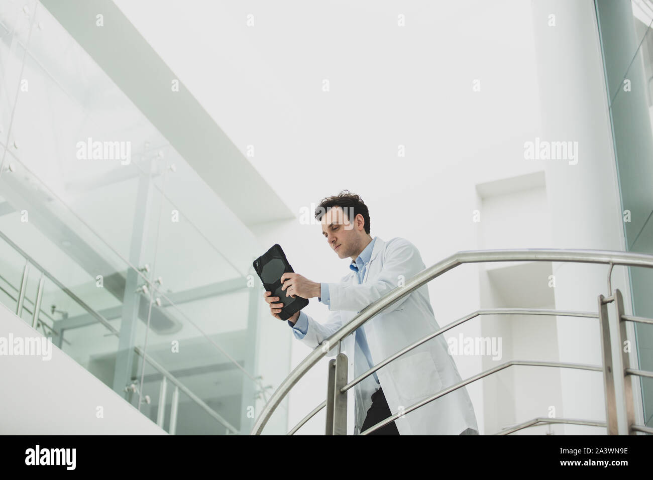 Maschio di medico in ospedale guardando i risultati dei test su una tavoletta digitale Foto Stock