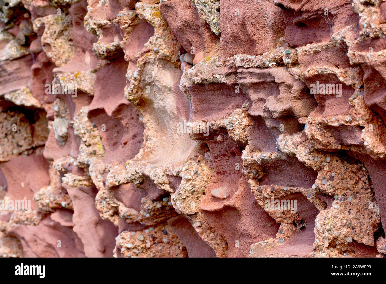 Un immagine astratta di un vecchio muro, dove il soft red di blocchi di pietra arenaria sono stati erodendo la via più veloce del più duro della malta di cemento. Foto Stock