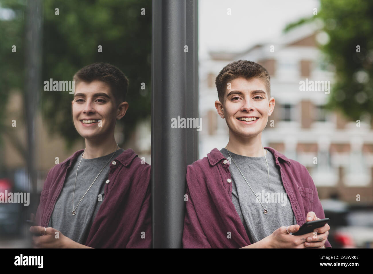 Ritratto di genere neutro giovane adulto con lo smartphone Foto Stock