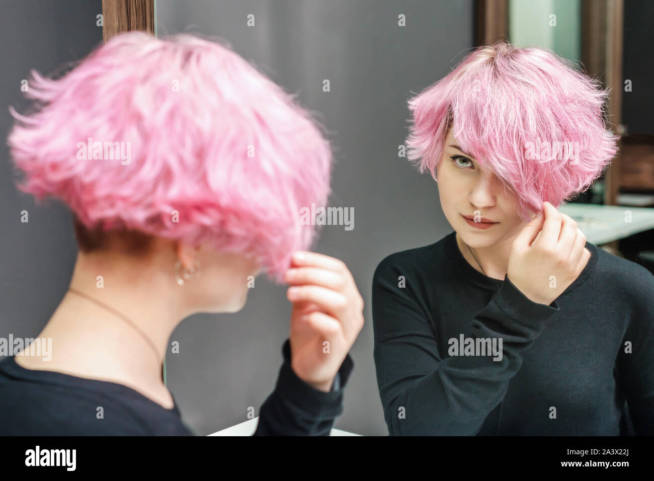 Capelli rosa donna con capelli corti sta guardando lo specchio. Concetto di bellezza. Foto Stock