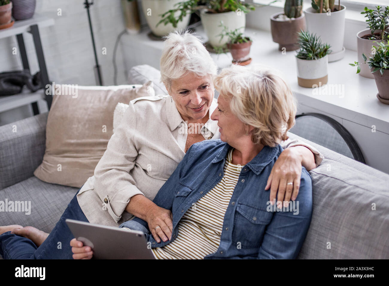 Coppia lesbica matura guardando a tavoletta digitale insieme sul divano Foto Stock