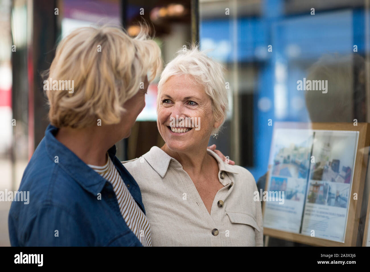 Coppia lesbica matura guardando agenzia immobiliare finestra Foto Stock