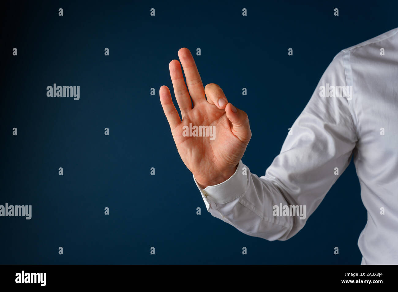 La mano di un uomo di affari rendendo un ok o eccellenti mano segno. Su sfondo blu scuro con copia spazio. Foto Stock