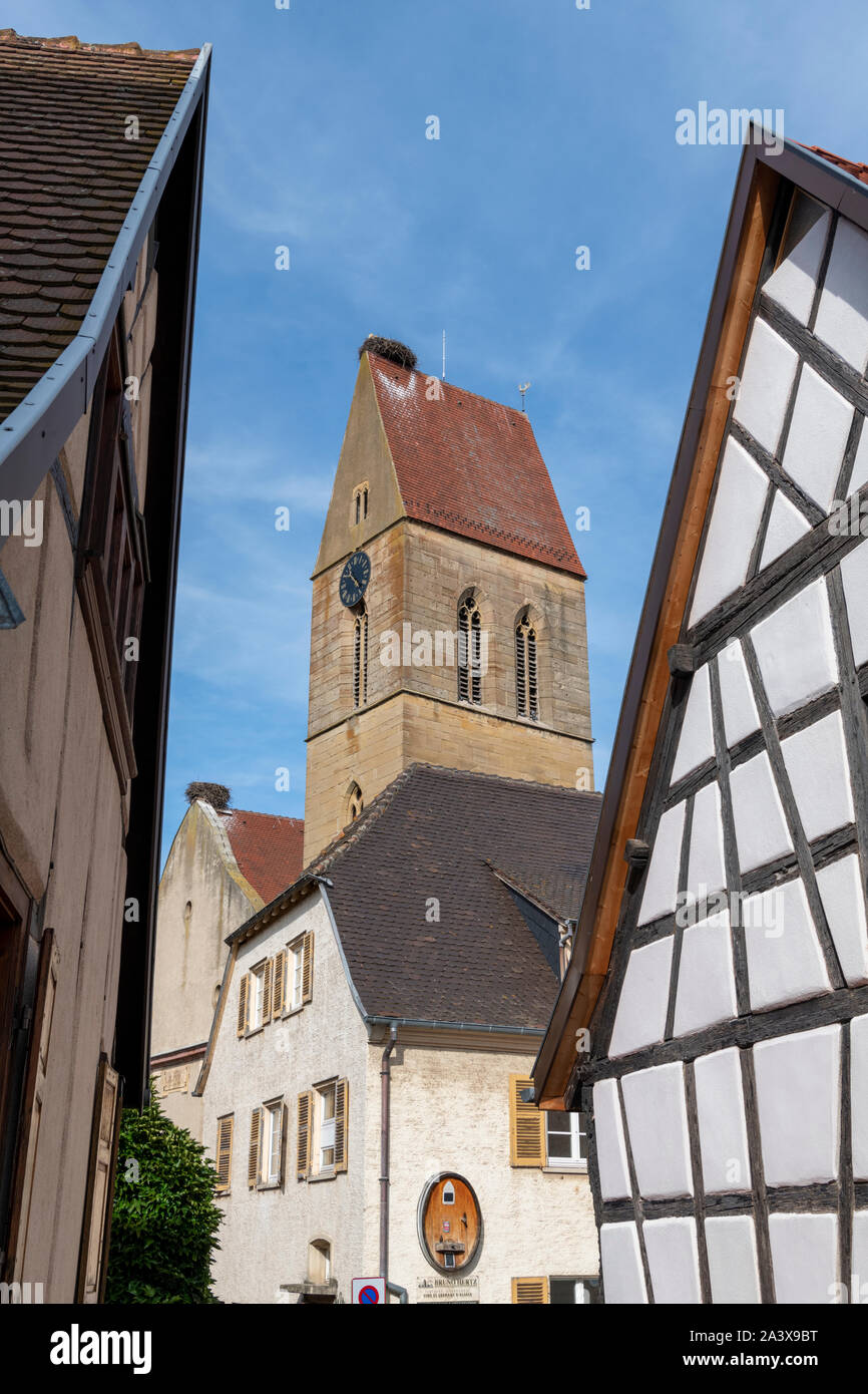 Una vista del campanile di una chiesa con un nido di cicogna sulla parte superiore attraverso il graticcio di vecchi edifici in Eguisheim Alsace Francia Foto Stock