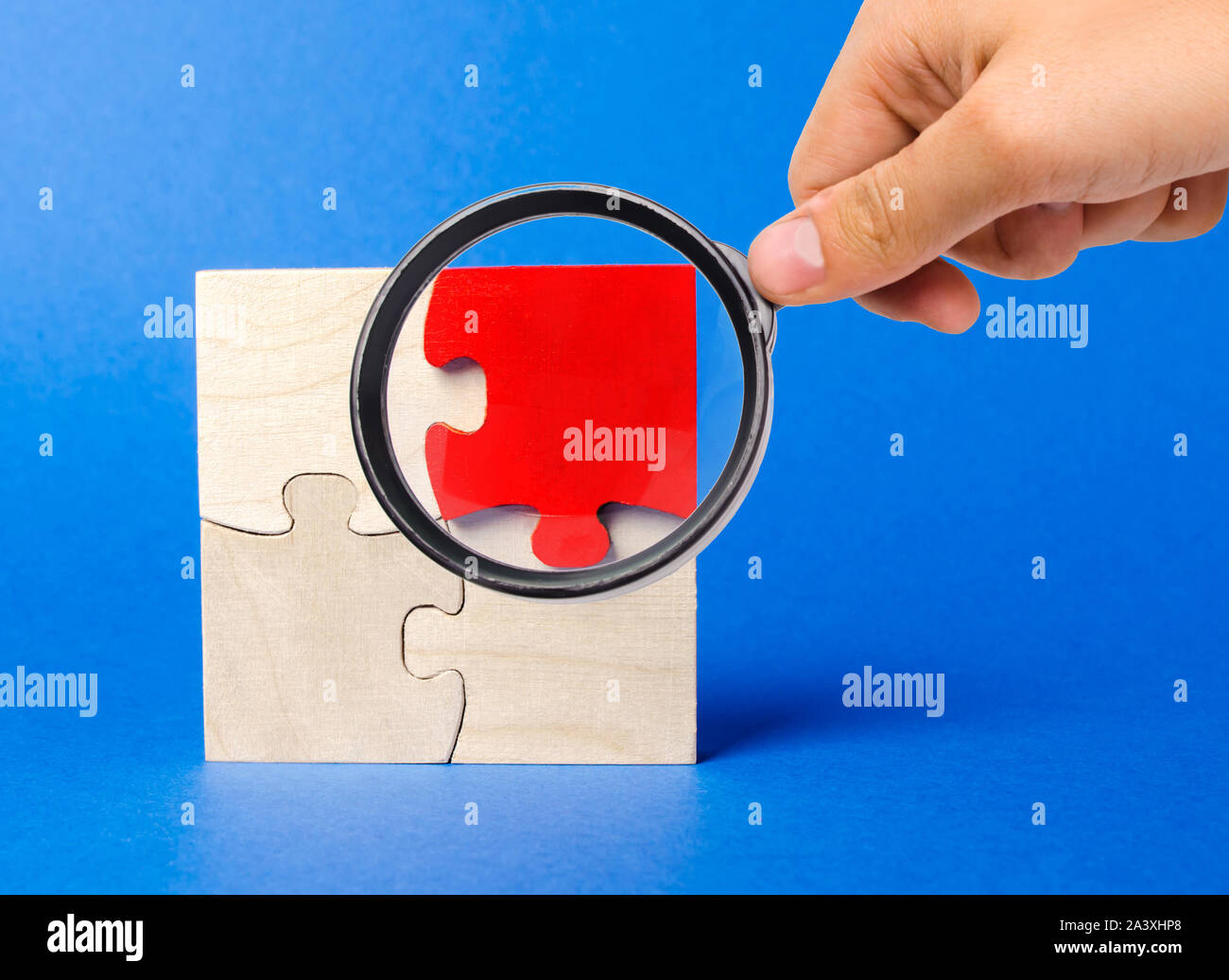 Una lente di ingrandimento appare in un rosso puzzle in legno su uno sfondo blu. Parere individuale. Distinguiti dalla folla. Unicità. Le divergenze di opinioni. Diff Foto Stock