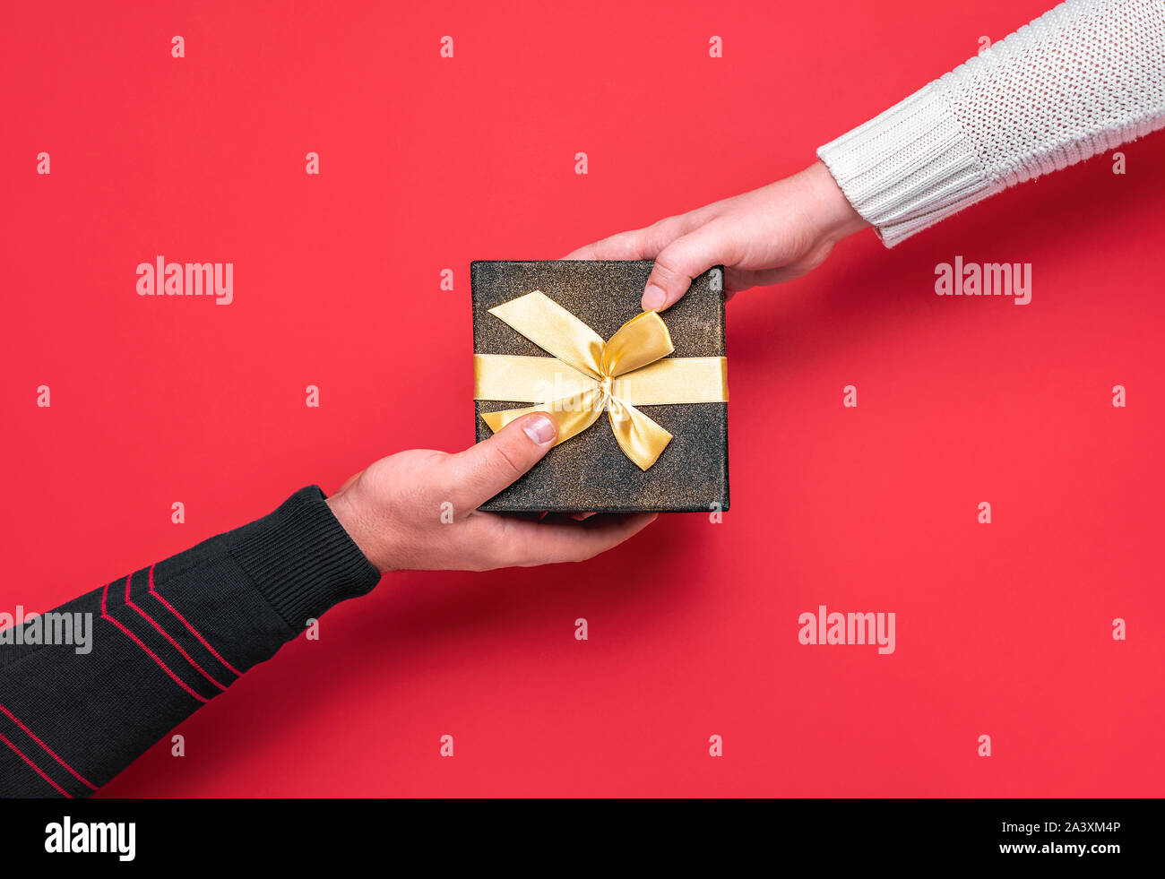 Dare e ricevere dono festivo box. Regali di natale il concetto di tempo. L uomo e la donna le mani su una confezione regalo nera su sfondo rosso. Regalo di natale di exchange. Foto Stock