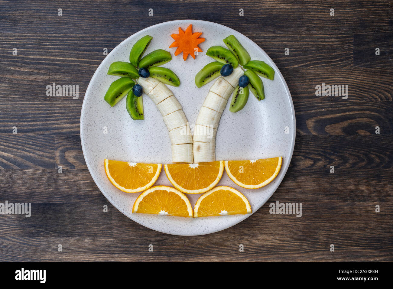 Creative dessert di frutta con kiwi, banana, uva, carota e arancione. Concetto di alimenti per bambini. Divertimento e sana insalata di frutta per bambini. Palme forma resa Foto Stock