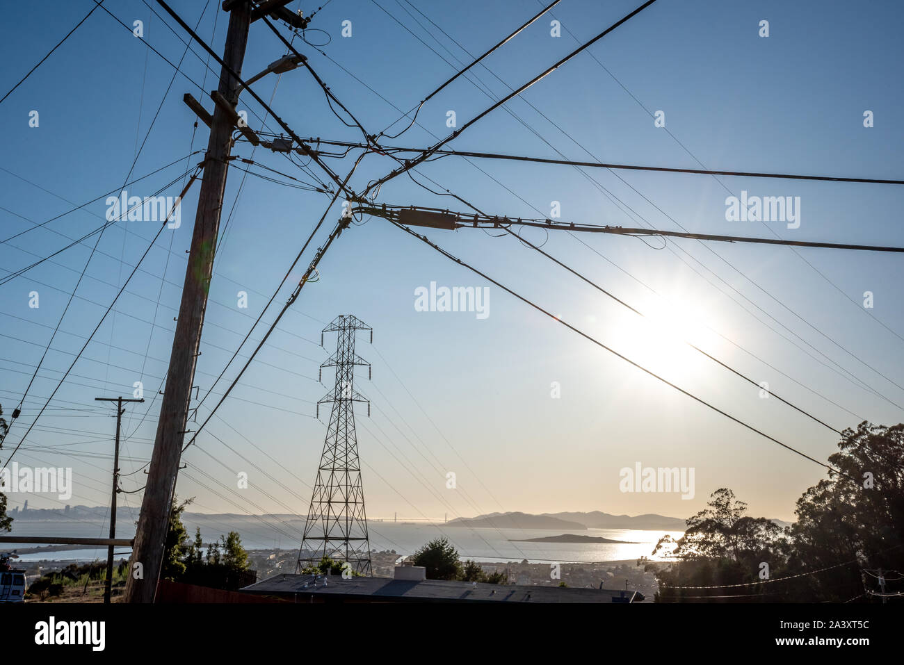 Sole splende attraverso le linee di alimentazione collegato ad un polo che incornicia un PG&E torre del trasformatore con la Baia di San Francisco e il Golden Gate Bridge in background. Foto Stock