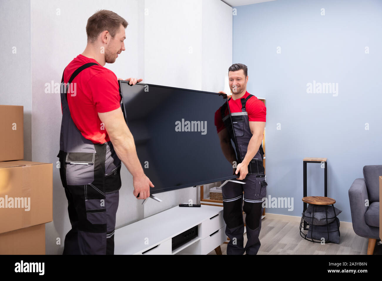 Due maschio Professional Movers In Uniforme lo scarico di televisione LCD in salotto Foto Stock