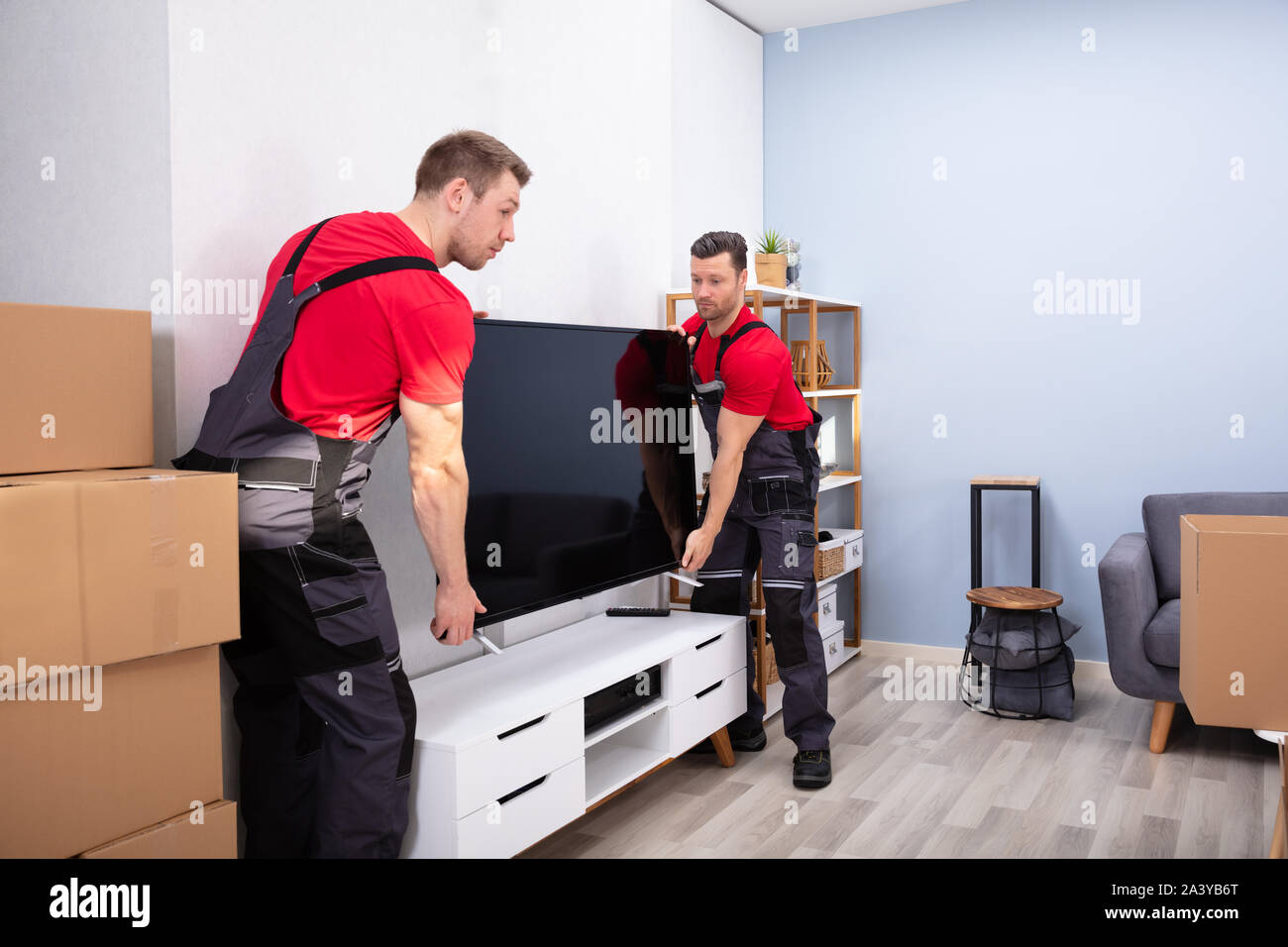 Due maschio Professional Movers In Uniforme lo scarico di televisione LCD in salotto Foto Stock