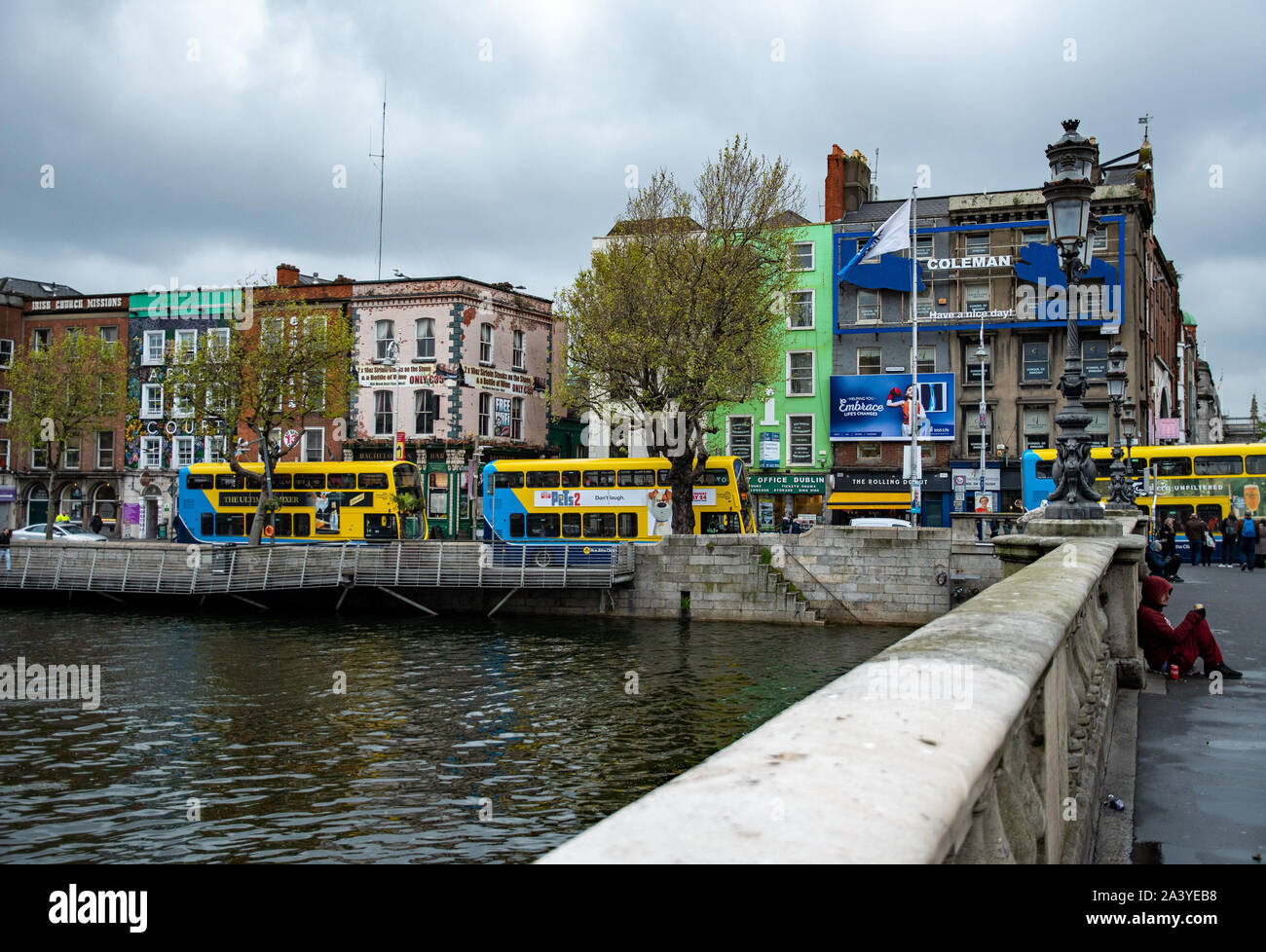 Edifici e ponti sul fiume Liffey, gente e autobus turistici tipici della città in una giornata nuvolosa. Dublino, Irlanda. Foto Stock
