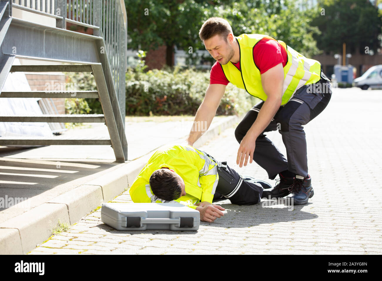 Preoccupato per il giovane uomo indossando giacca di sicurezza guardando alla persona che cade sulla strada con la cassetta degli attrezzi Foto Stock