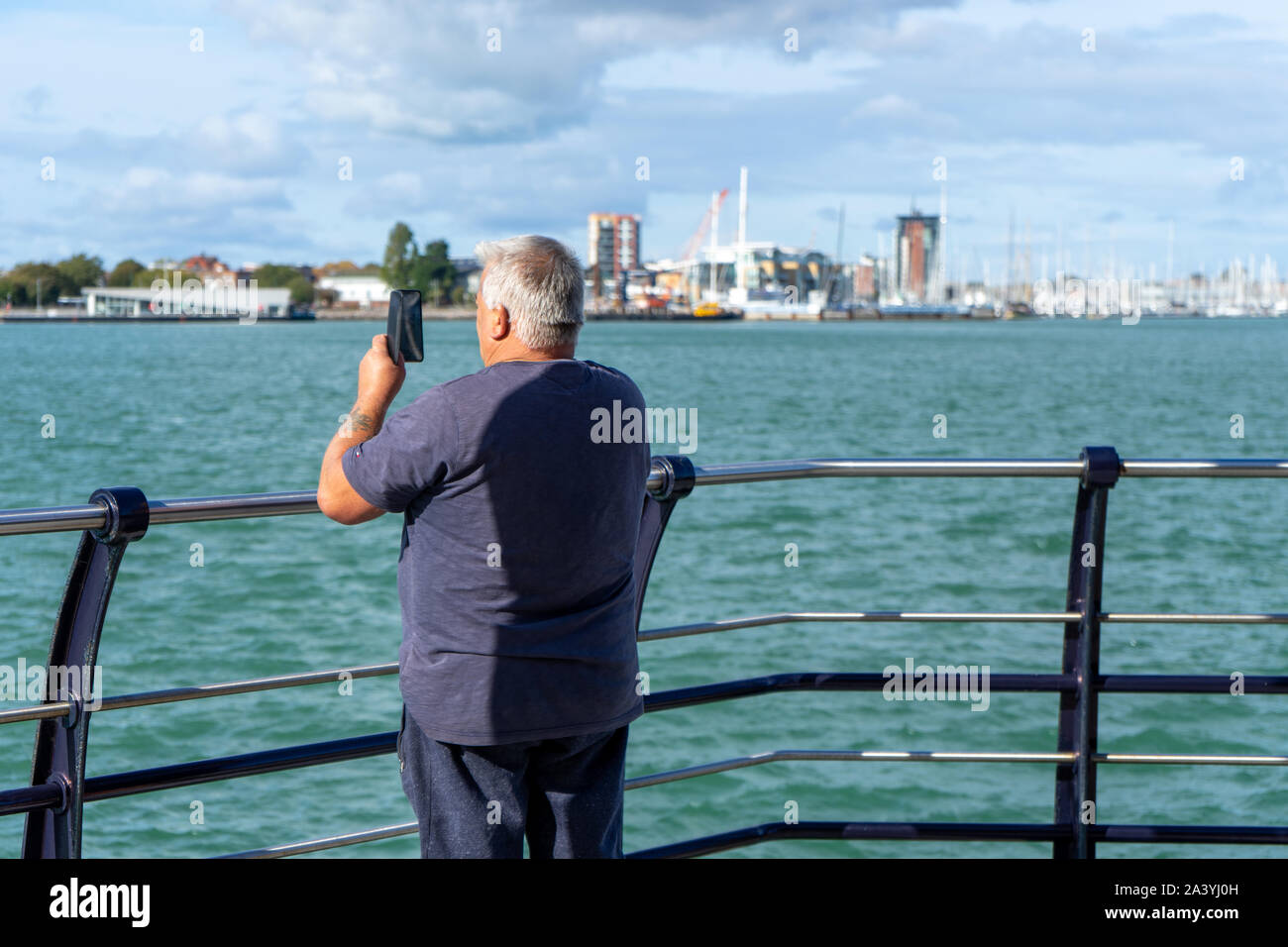 Un uomo di mezza età di scattare una foto al mare con il suo telefono cellulare o telefono cellulare Foto Stock