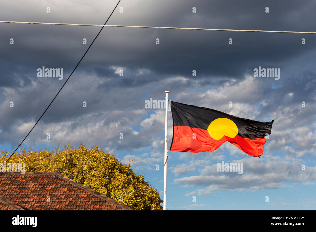 Bandiera aborigena battenti alto sopra un centro comunitario nella zona suburbana. Foto Stock