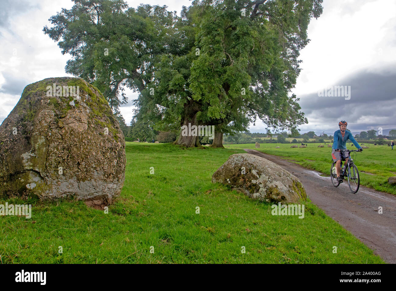 Ciclista a cavallo tra le pietre del Long Meg Stone Circle - La costa a costa percorso ciclabile passa a poche centinaia di metri da Long Meg Foto Stock