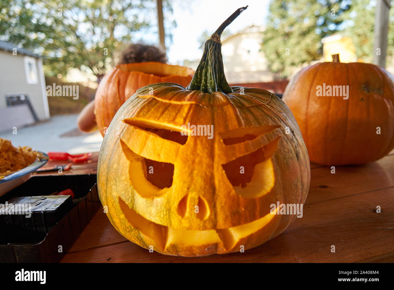 Tre le zucche su una tavola di legno per la festa di Halloween. Il più vicino uno ha un volto scolpito in esso. La polpa di zucca è visibile sulla sinistra. Foto Stock