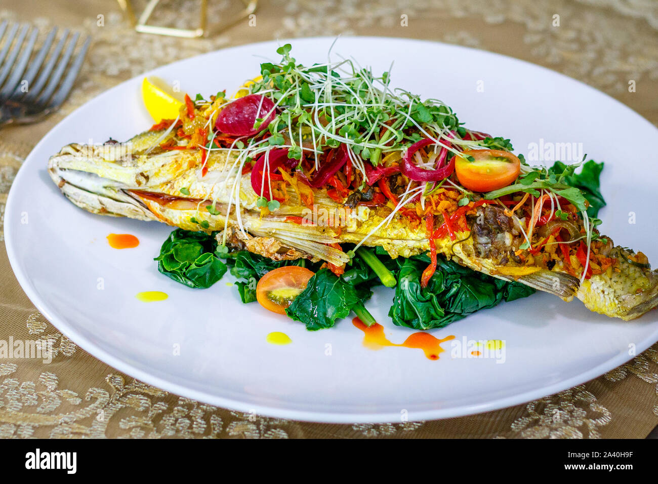 Tutto il Baby Barramundi con Kai-lan (broccoli cinesi), peperoncino, lo Zenzero Curcuma, coriandolo e limone. Decorate con cipolla colorata con succo di barbabietola. Foto Stock