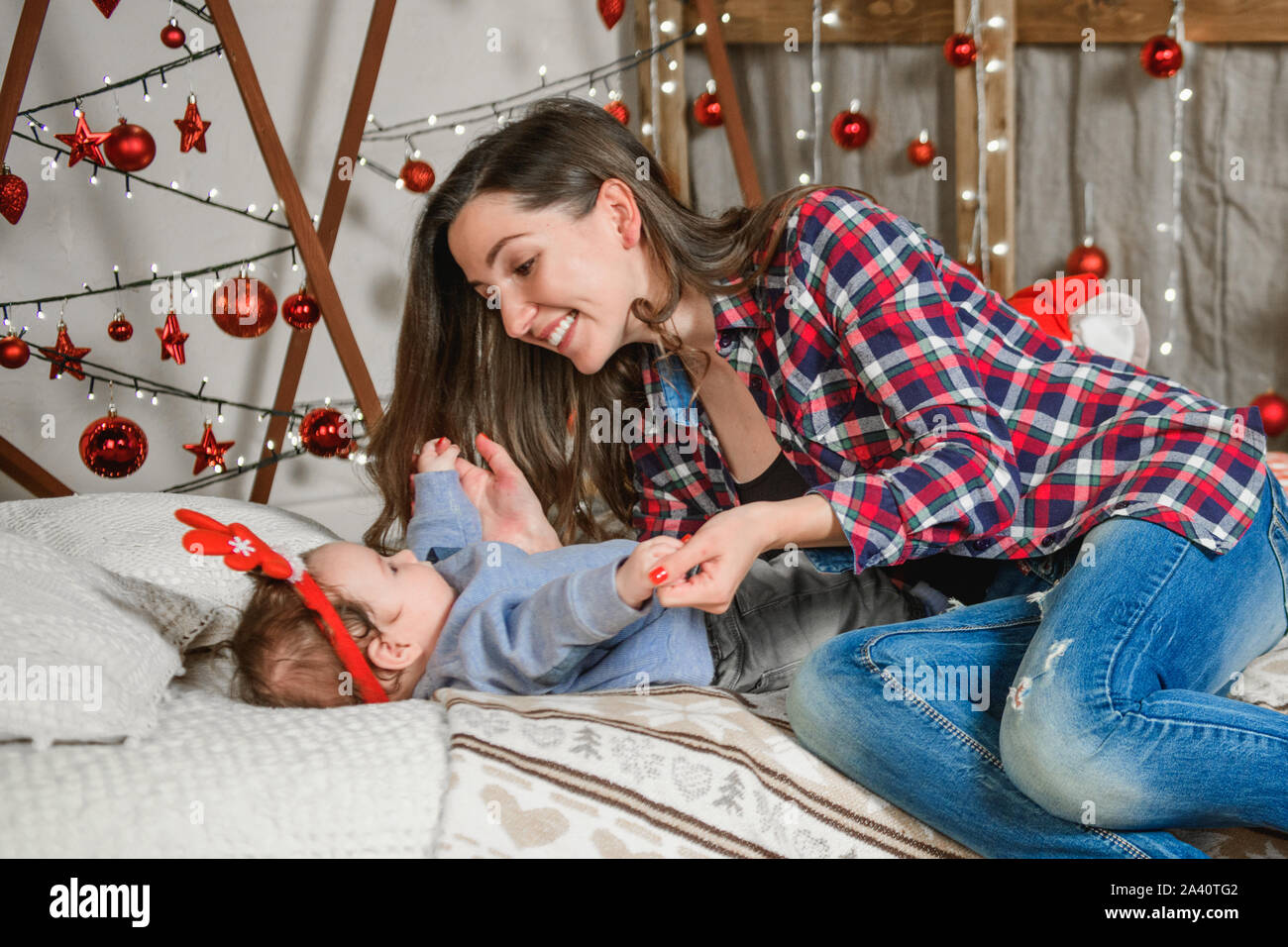 La mamma con un bambino su un sfondo di Natale. red corna sulla testa di un piccolo bambino. Anno nuovo. Celebrazione della Messa di Natale Foto Stock
