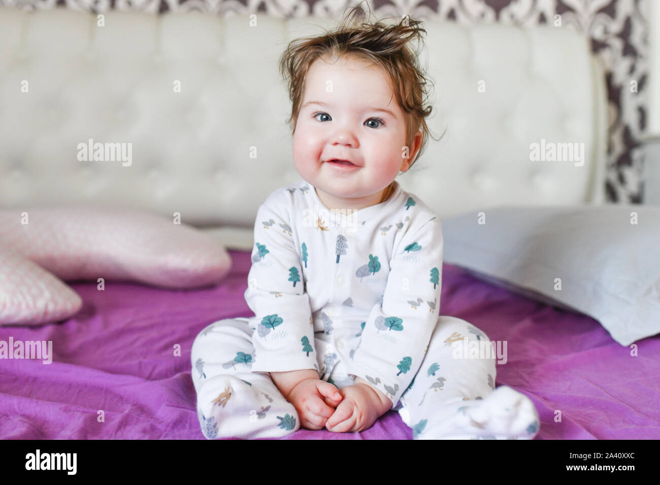 Baby in posa su telecamera seduta sul letto. Il bambino gioca in biancheria da letto. Foto Stock