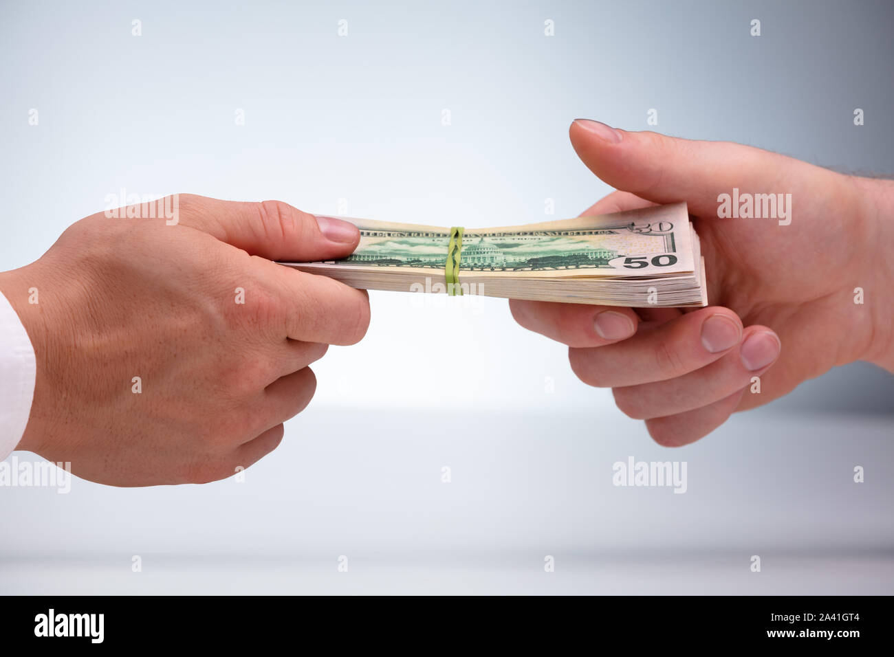 Close-up di due maschi della mano azienda Bundle valuta legato con gomma elastica contro uno sfondo grigio Foto Stock