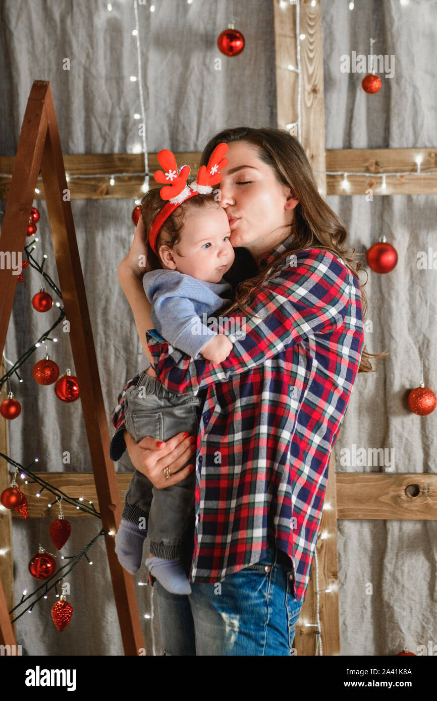 La mamma con un bambino su un sfondo di Natale. red corna sulla testa di un piccolo bambino. Anno nuovo. Celebrazione della Messa di Natale Foto Stock