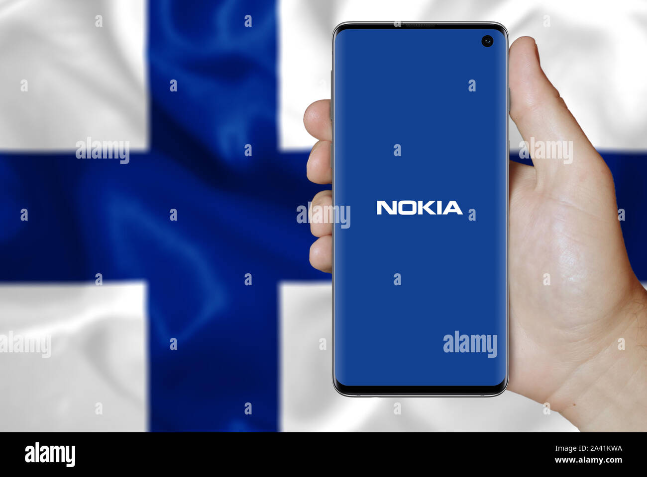 Un uomo detiene un telefono visualizzando il logo di Nokia società elencate su OMX Helsinki. Flag di fine dello sfondo. Credito: PIXDUCE Foto Stock