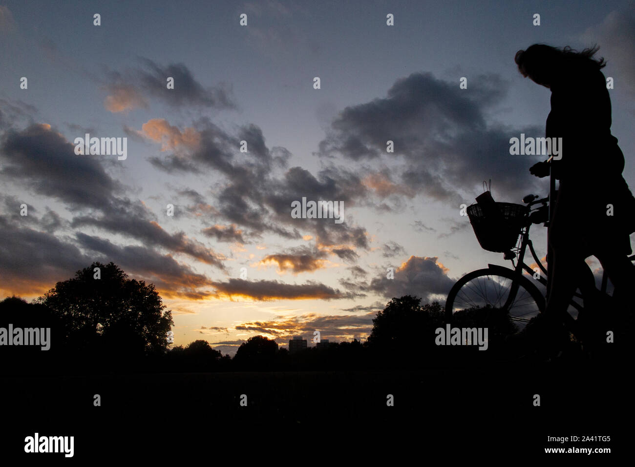 Un ciclista passeggiate home sotto un tempestoso tramonto in un parco di Londra Foto Stock