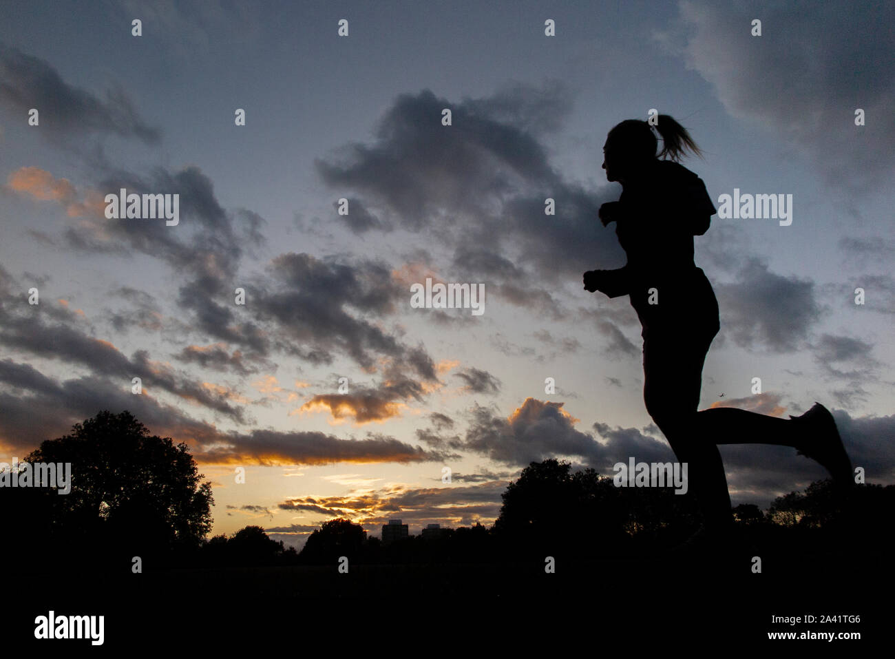 Un pareggiatore femmina corre home sotto un tempestoso tramonto in un parco di Londra Foto Stock