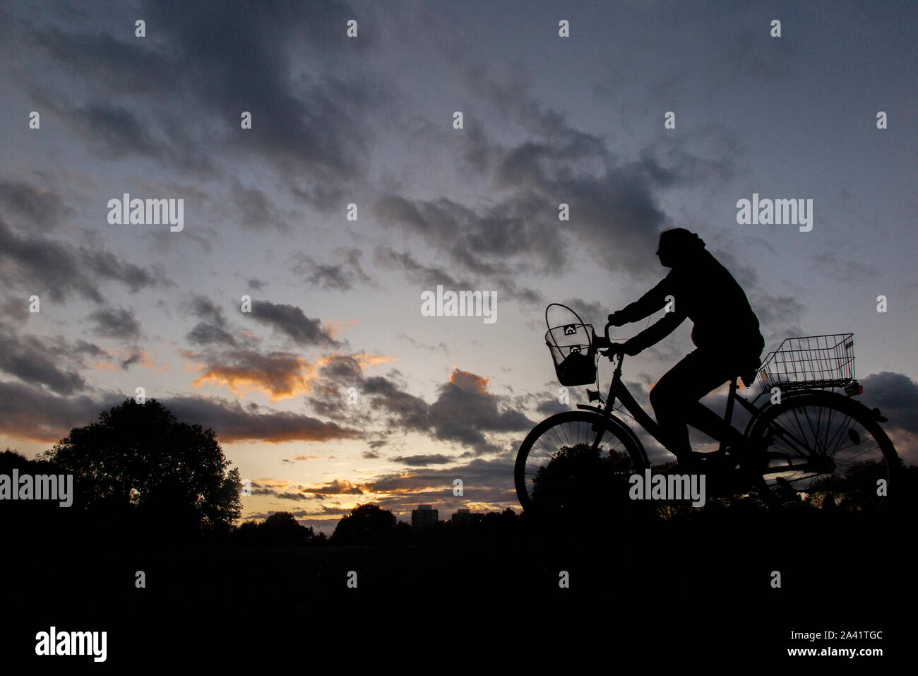 Un ciclista rides home sotto un tempestoso tramonto in un parco di Londra Foto Stock