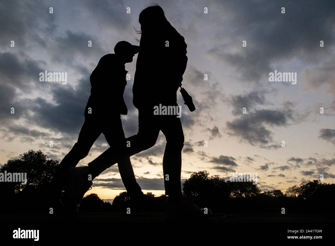 Un paio a casa a piedi sotto un tempestoso tramonto in un parco di Londra Foto Stock