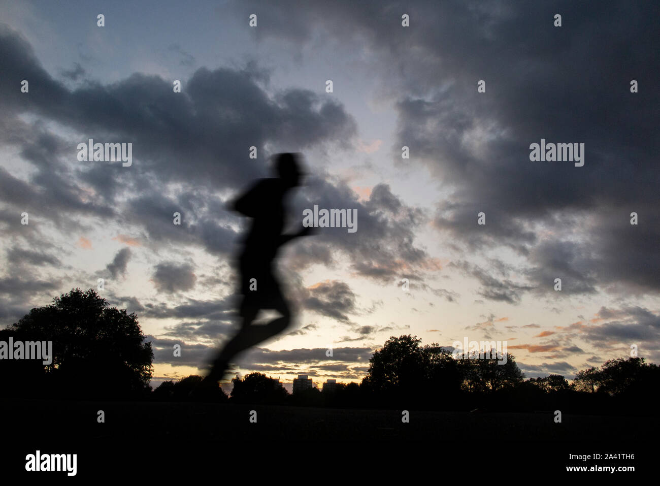 Un runner fa avanzare home sotto un tempestoso tramonto in un parco di Londra Foto Stock